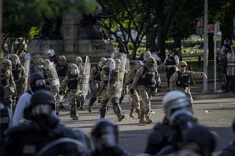 People in military uniforms walk into an open paved area.